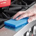 A person's gloved hand cleaning a stove top with a blue sponge.