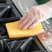 A hand in a plastic glove using a yellow sponge to clean a kitchen counter.