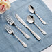 Acopa Swirl stainless steel flatware set on a blue cloth with a napkin.