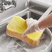 A hand in a glove using a Lavex jumbo sponge to wash a dish.