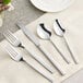 Acopa Penn Square stainless steel flatware set on a white cloth with a fork and spoon.