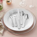 A white plate with an Acopa Triumph stainless steel spoon and fork on it.