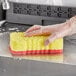 A hand in a glove using a yellow Lavex sponge to clean a sink.