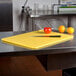 A yellow San Jamar cutting board on a counter with a knife and yellow and orange fruits.