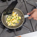 A hand holds a blue Vollrath Wear-Ever fry pan with scrambled eggs and vegetables.