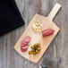 An American Metalcraft wood serving peel with meat and olives on a wood surface.