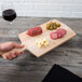 A hand holding an American Metalcraft wood serving peel with food on it over a table set with a glass of red wine.