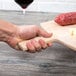 A hand holding an American Metalcraft wood serving peel with meat and cheese on it.