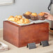 A person using an Acopa wood display riser to hold a plate of pastries including a croissant.