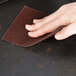 A hand using a Winco grill screen to clean a brown surface.