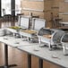 A metal Choice Deluxe roll top chafer on a buffet table with food.