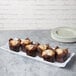A white rectangular melamine tray with scalloped edges holding muffins on a bakery display counter.