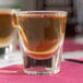 A Libbey shot glass filled with brown liquid on a table in a bar.