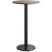 A Lancaster Table & Seating bar height table with a round reversible birch and ash top on a cast iron base with a black pole.