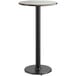 A round Lancaster Table & Seating bar height table with a reversible black and brown laminated top on a black cast iron base.