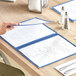 A hand holding a blue Choice trifold menu on a table.