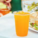 A plastic cup of orange Sqwincher electrolyte drink with ice on a table next to a sandwich.