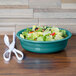 A Fiesta turquoise china bowl filled with salad on a wood table with a pair of white scissors.