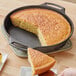 A hand uses a knife to cut a piece of cornbread out of a Lodge cast iron skillet.