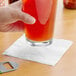 A hand holding a glass of beer with a EcoChoice bamboo beverage napkin on a table.