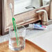 An Oral-B Sensi-Soft toothbrush in a glass on a counter.