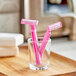 Two pink Gillette Daisy razors in a glass on a wooden tray.