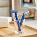 Two blue Gillette Sensor2 men's disposable razors in a glass on a wooden table.