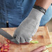 A person wearing a Schraf gray cut-resistant glove cutting carrots on a counter.