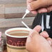 A hand using a white Royal Paper Stix To Go beverage plug and stirrer to stir coffee.