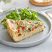 A slice of Priscilla's spinach, artichoke, and roasted red pepper quiche on a plate with greens.