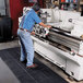 A man in a blue shirt and jeans using a Cactus Mat connectable anti-fatigue floor mat while working on a machine.