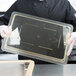 A person holding a Cambro clear plastic food storage box lid.