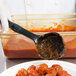 A person using a Vollrath High Heat Solid Oval Nylon Spoodle to serve meatballs with red sauce.