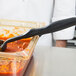 A chef uses a Vollrath High Heat Solid Oval Nylon Spoodle to stir red sauce in a glass container.