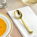 A gold Visions plastic soup spoon on a white napkin.