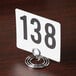 An American Metalcraft chrome swirl base table card holder with a white card and black numbers in it.