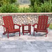Two red faux wood Adirondack chairs with a table on a stone patio.