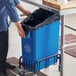 A person pushing a Lavex blue rectangular recycling bin under a counter.