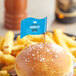 A burger with a medium wavy flag pick on top sits on a plate of fries.