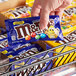 A hand holding a small package of M&M's Caramel Milk Chocolate candies.