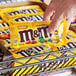 A hand holding a package of M&M's Peanut Milk Chocolate Candies.