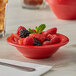 A close up of a red Thunder Group melamine salad bowl filled with fruit and berries.