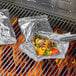 Two foil packets of food cooking on a grill.