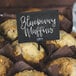 Blueberry muffins with a close-up of a black chalk card that says blueberry muffins on a table in a bakery display.