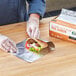A person in gloves wrapping a sandwich in a Choice box of foil sheets.