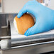 A person in blue gloves using an APW Wyott Vertical Conveyor Bun Grill Toaster to toast a roll.