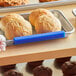 A person using a Baker's Mark blue silicone bun pan clip to identify a tray of rolls.