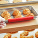 A gloved hand uses a red Baker's Mark tray to hold a tray of baked goods in a bakery display.