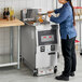 A woman using a Henny Penny natural gas fryer to cook food in a commercial kitchen.