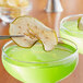 A glass of green liquid with a dried Granny Smith green apple slice on top.